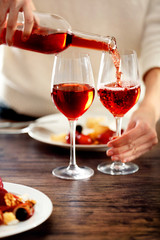 Young woman pouring pink wine into glass on the table