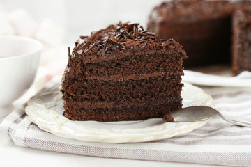 Sliced chocolate cake on wooden table, on light background