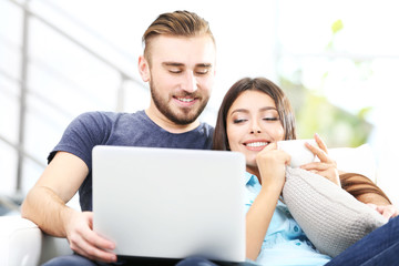 Fototapeta premium Szczęśliwa para siedzi na kanapie z kawą i pracuje na laptopie