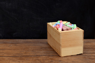Wooden box of coloured chalk in front of blackboard