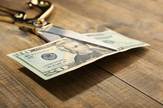 Scissors cuts dollar banknote on wooden background