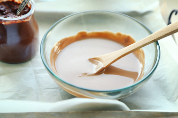 Melted chocolate on glass bowl on tray, on wooden background