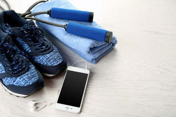 Sport shoes, towel and smart phone on wooden background