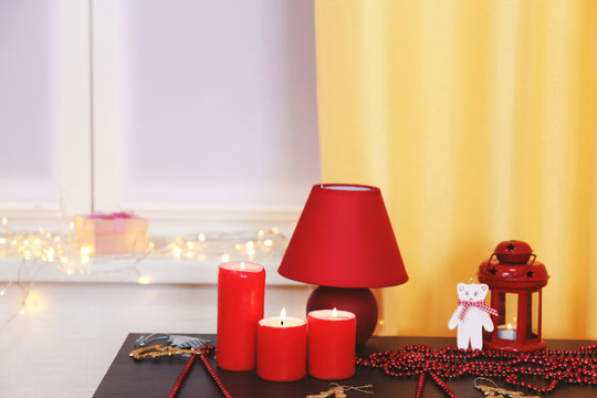 Colourful Christmas decorations and candles on the table against window decorated with glowing lights, close up