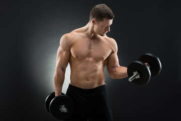 Fototapeta na wymiar Determined Muscular Man Exercising With Dumbbells