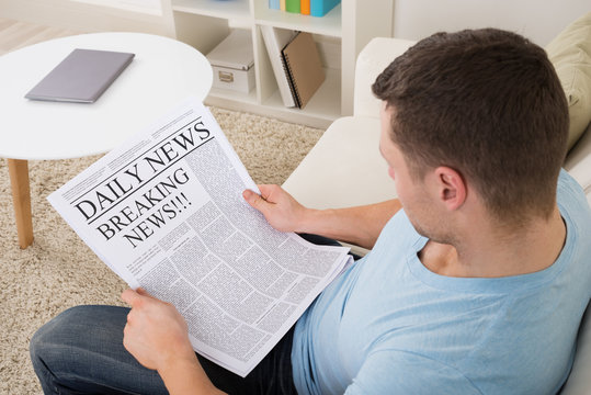 Man Reading Breaking News On Newspaper At Home