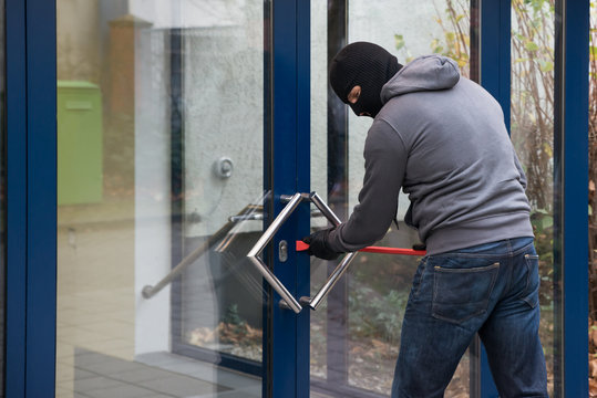 Man Using Crowbar To Open Glass Door