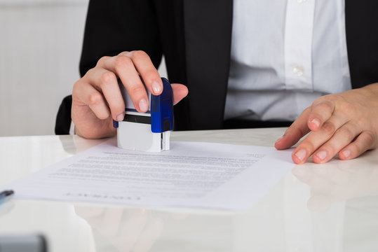 Businesswoman Stamping Contract Document At Desk