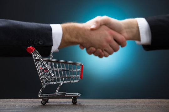 Shopping Cart On Table With Businessmen Shaking Hands