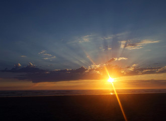 Obraz na płótnie Canvas Cloudy Sunset Over the Ocean with Sunbeams in the Sky