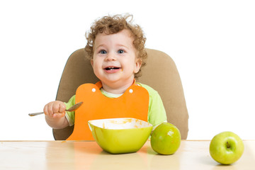 little child eats with spoon sitting at table with fruits 