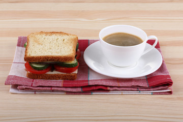 a sandwich of toast with tomatoes and cucumber with cheese on napkin on wooden table with Cup of coffee