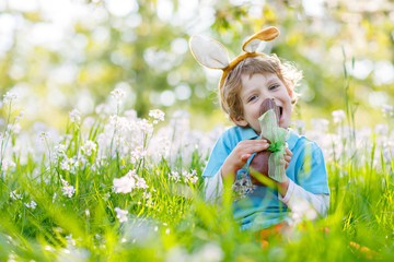 Little kid boy eating chocolate Easter bunny outdoors