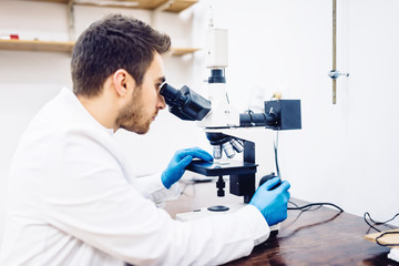 Naklejka na ściany i meble man, male scientist, chemist working with microscope in pharmaceutical laboratory, examining samples