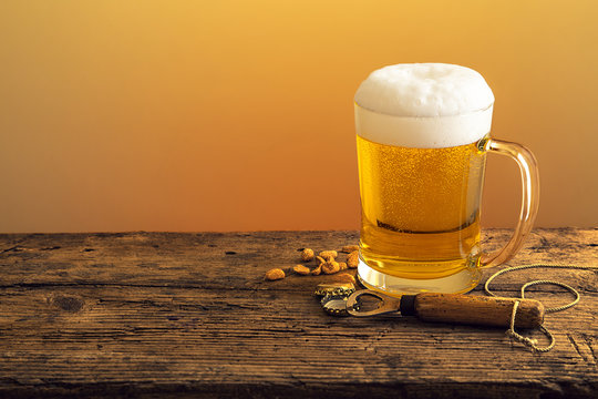 Bierkrug mit Bier und Schaumkrone mit Flaschen&ouml;ffner auf Holztheke
