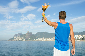 Athlete in athletic uniform standing with sport torch in front of Rio de Janeiro Brazil skyline at...
