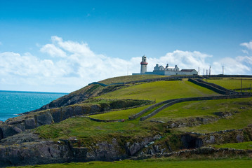 Fototapeta na wymiar Irish cliff with greenery and a lighthouse in the distance - Coastline of Cork