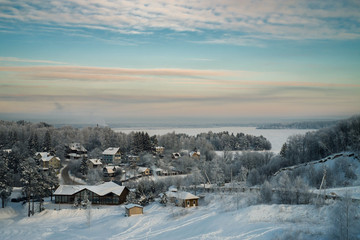 Fototapeta na wymiar Snowy forest and cottages and iced lake at sunset