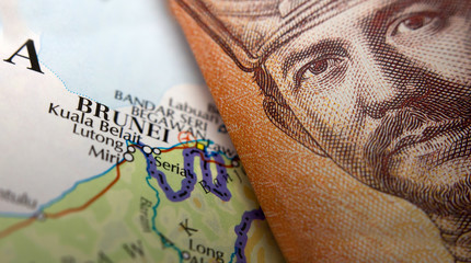 Folded Brunei Currency on top of a map of Brunei
