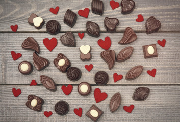 Fototapeta na wymiar Many chocolates and felt hearts on wooden plank.