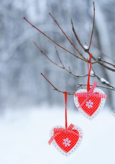 Red heart decoration detail handing on a tree in winter forest full of snow. Winter season holiday concept