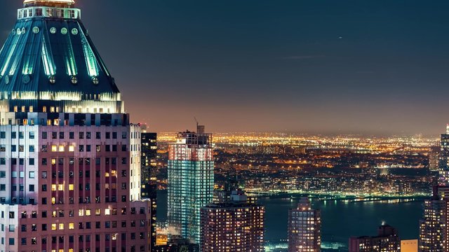 Midtown Manhattan skyline illuminated at night with a view of the Hudson River and One World Plaza in time-lapse