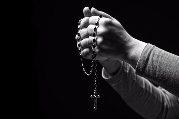 christian rosary in hands. black background. faith, religion, belief