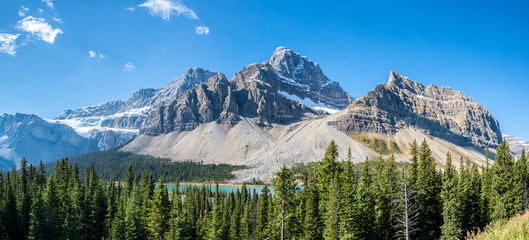 panoramic view of a lake with turquoise waters in the middle of a forest and some peaks of the rocky mountains of alberta canada