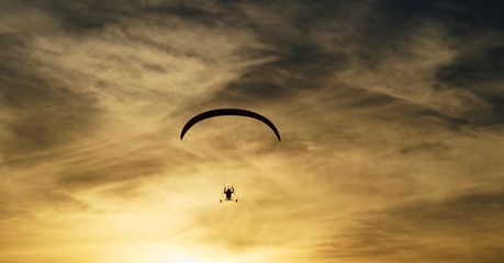 Paragliding in the clouds at sunset. Silhouettes against a background cloudy sky in the colors of the sunset.