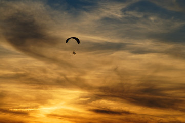 Paragliding high in the clouds at sunset. Silhouettes against a background cloudy sky in the colors of the sunset.