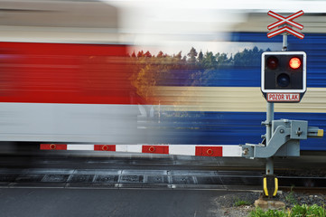 Motion blur speeding passenger train passing through a railway crossing with gates.