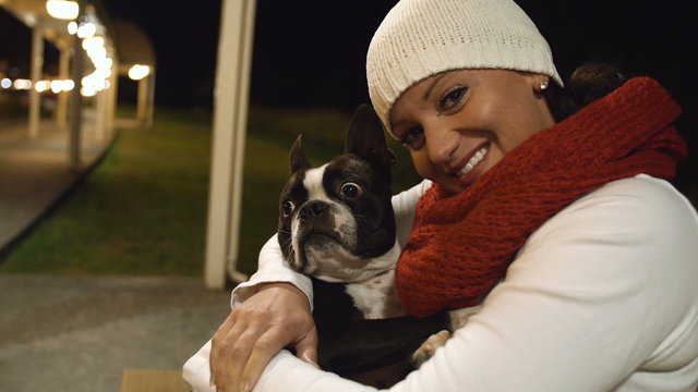 Woman Hugging Dog Outdoors. Pretty Young Woman Smiling with Boston Terrier in City at Night