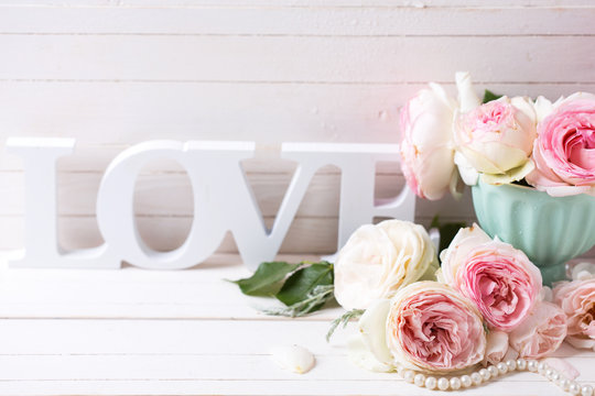 Pink roses flowers in vase and word love  on white painted woode
