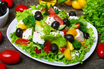 Greek salad with fresh vegetables, feta cheese and black olives on a wooden background