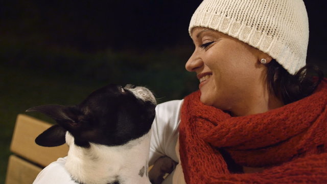 Woman on Bench with Dog. Pretty Young Woman Smiling with Boston Terrier Outdoors at Night