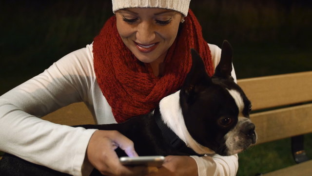 Woman with Dog on Smartphone. Young Woman with Boston Terrier on Cell Phone at Night Outdoors