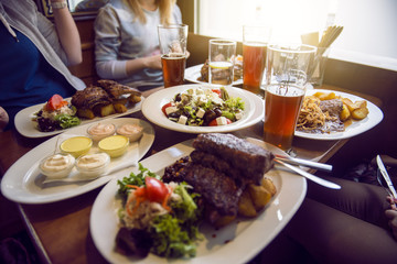 Friends having a dinner in the restaurant with salad, barbeсue and beer