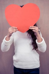 Woman hiding her face behind paper heart