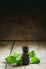 Essential oil of peppermint in a small brown bottle with fresh g