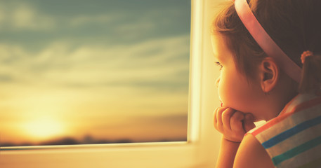child sad little girl looking out window at sunset - Powered by Adobe