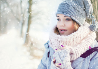 Beautiful  young woman wearing winter hat gloves and scarf covered with snow flakes. Winter forest landscape background