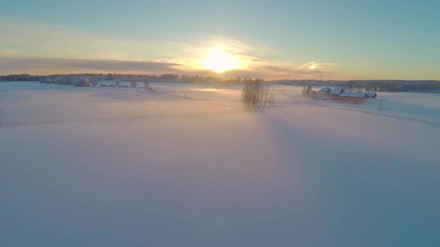 Flying above foggy fields with snow in sunset