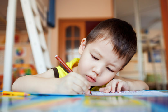 The boy carefully and intently draws in a special notebook for drawing, education at home, pre-school training, development of children creative abilities. Classroom.