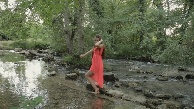 Smiling girl in a bright pink dress walking barefoot on the water of the river