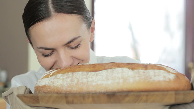 Young woman smelling freshly baked bread in kitchen, close up
