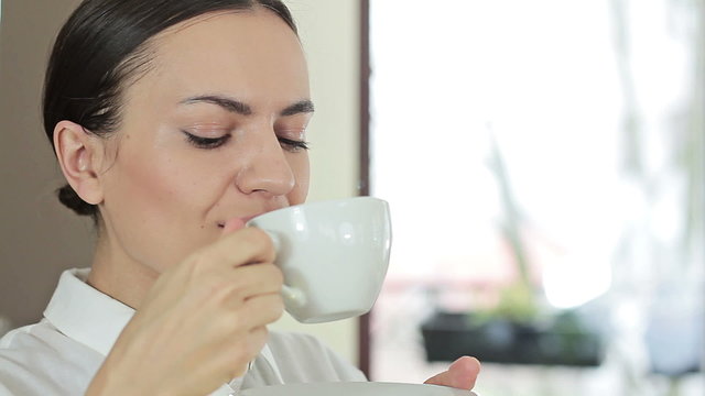 Portrait of young brunette woman drinking coffee at home in the morning, close up
