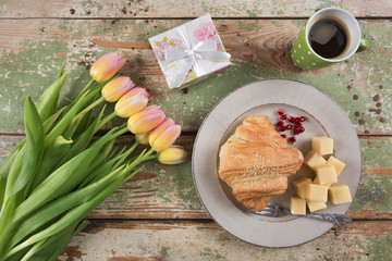 Breakfast, cup of coffee, bouquet of tulips and gift box on wooden table