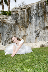 smiling little girl with white dress near the waterfall