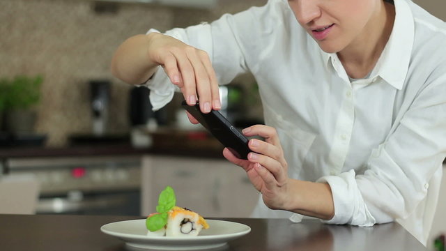 Woman with smartphone taking picture of sushi at restaurant