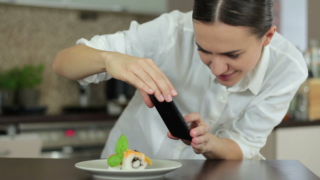 Woman with smartphone taking picture of sushi at restaurant